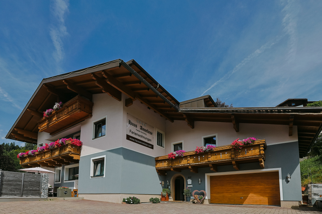 Außenansicht von Haus Anneliese mit Holzbalkonen, Blumen und Garage unter blauem Himmel